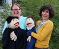 Diakonin Tanja Götz und Pfarrerin Annika Landt mit zwei Handpuppen vor der Pauluskirche.